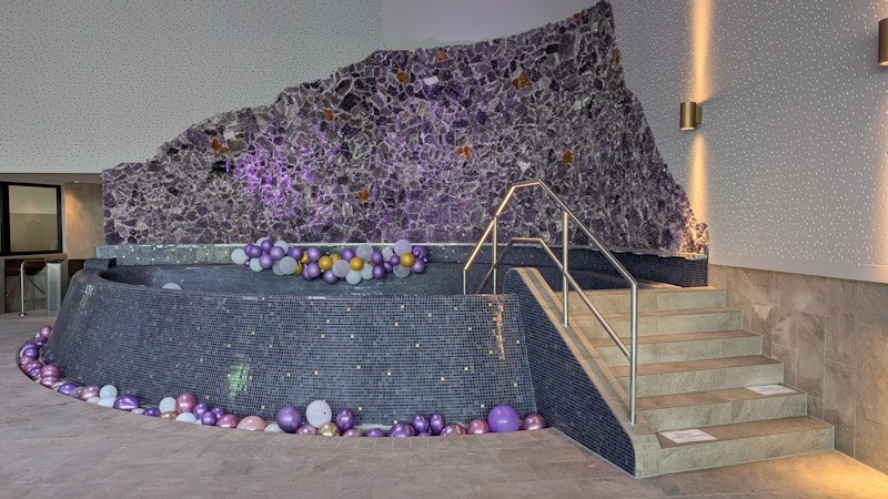 PXL_20260701_082136586.MP Beleuchtete Amethystwand mit geschwungenem Mosaikbecken und gefliestem Treppenaufgang im Miramar Weinheim