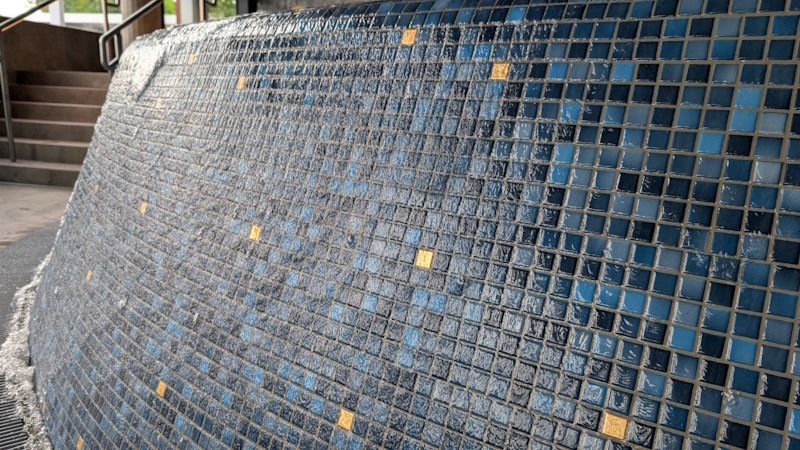 PXL_20260701_082426741.MP Nahaufnahme der blauen Glasmosaikfliesen mit einzelnen goldfarbenen Mosaiksteinen am Beckenrand